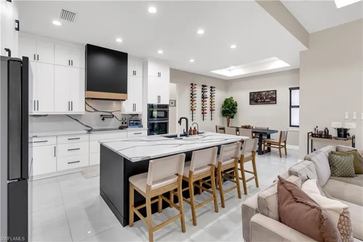 Two tone kitchen with a kitchen breakfast bar, light stone countertops, a center island with sink, black appliances, and modern cabinets