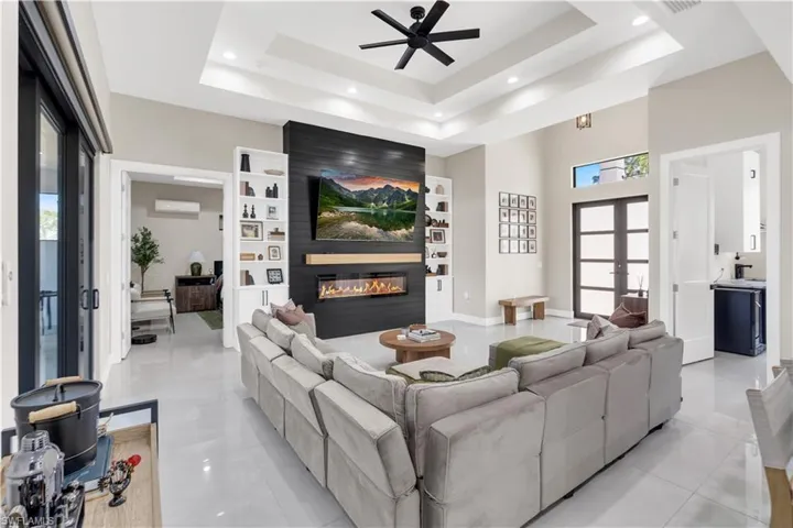 Living room with a ceiling fan, plenty of natural light, a large fireplace, a high ceiling, and built in shelves