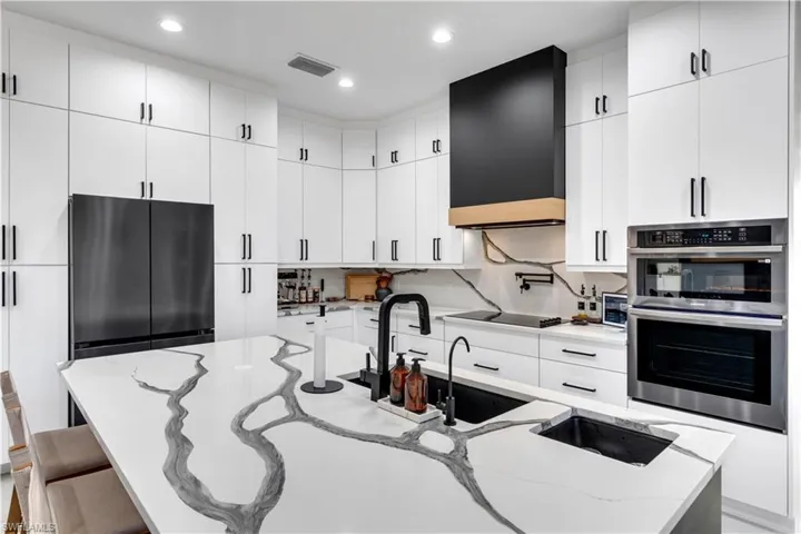 Kitchen with stainless steel appliances, a kitchen island with sink, light stone countertops, white cabinetry, and recessed lighting