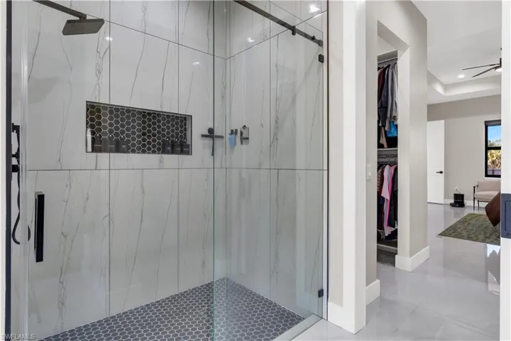 Full bathroom with a marble finish shower, a walk in closet, ceiling fan, tile patterned flooring, and a raised ceiling