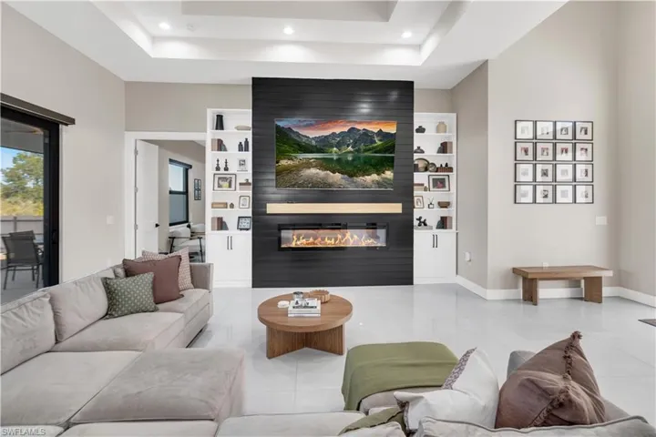 Living area with tile patterned floors, a large fireplace, recessed lighting, built in shelves, and a raised ceiling