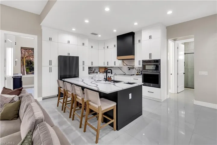 Dual tone kitchen with a center island with sink, a breakfast bar area, double oven, light stone countertops, and two tone cabinetry