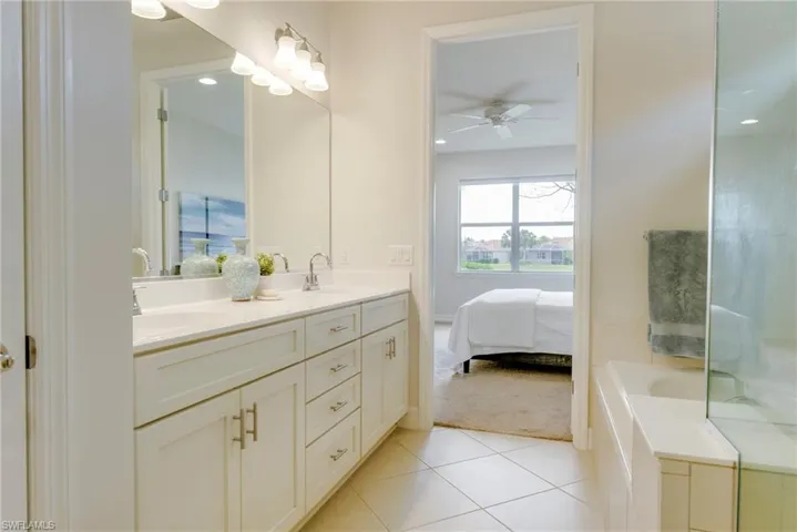 Bathroom featuring ceiling fan, tiled bath, double vanity, and tile patterned floors