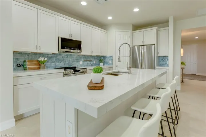 Kitchen with appliances with stainless steel finishes, tasteful backsplash, an island with sink, white cabinets, and light tile patterned floors