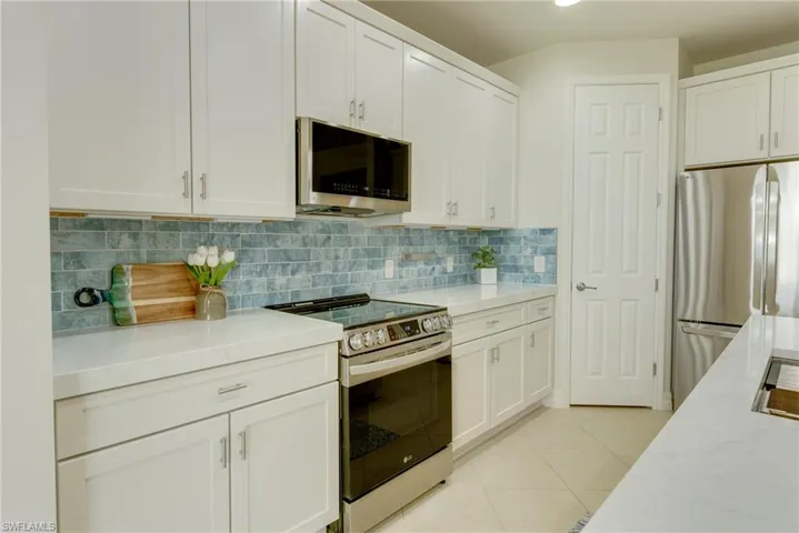 Kitchen with white cabinetry, light stone counters, decorative backsplash, light tile patterned floors, and stainless steel appliances