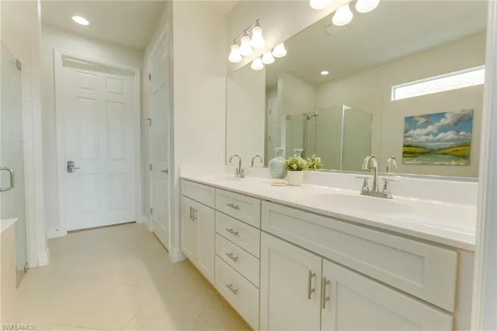 Bathroom featuring a shower with shower door, double vanity, and tile patterned floors