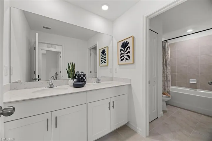 Dual sink vanity with white cabinetry and chrome hardware, a large wall-mounted mirror, and recessed lighting