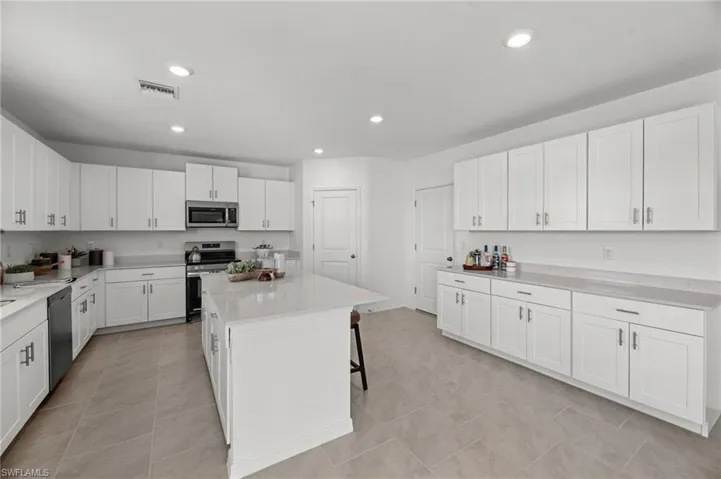 Spacious kitchen featuring an expansive island, white shaker cabinetry, light-toned countertops, tile flooring, and stainless-steel appliances
