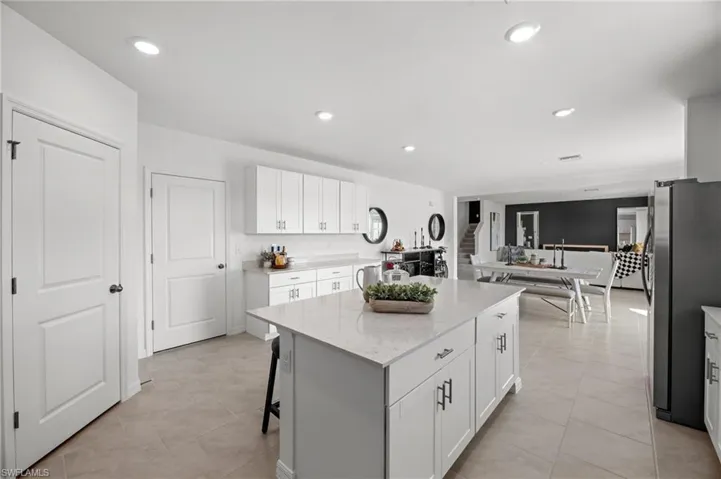 Recessed lighting, tile flooring, white shaker cabinetry, light-toned countertops, and a kitchen island with storage