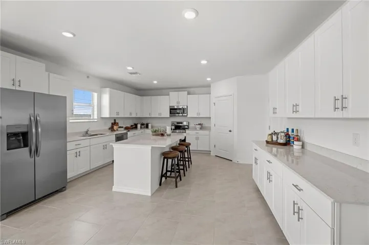 Contemporary kitchen featuring stainless steel appliances, a center island with seating, extensive white cabinetry, light-toned countertops, and tiled flooring