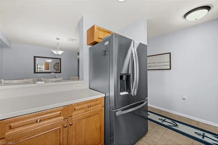 Kitchen area featuring wood cabinetry, light-colored countertops, a stainless steel refrigerator, and tiled flooring