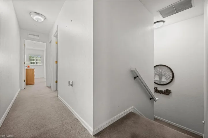 Carpeted hallway and staircase featuring light-colored walls, white trim, and flush-mount lighting fixtures