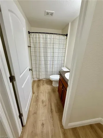 Full bathroom with visible vents, toilet, a textured ceiling, wood finished floors, and vanity