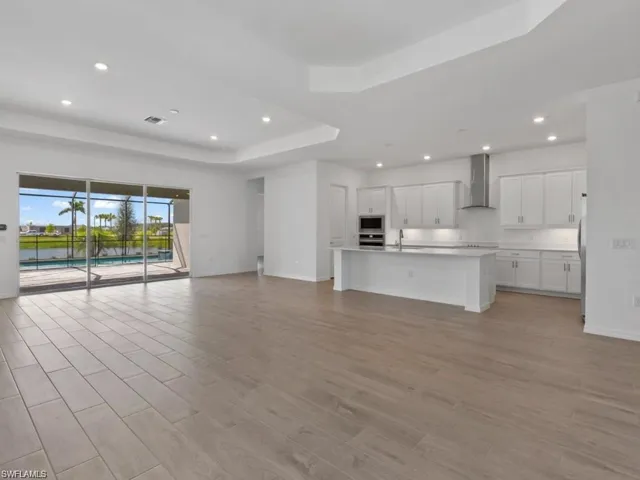 Unfurnished living room featuring baseboards, recessed lighting, light wood-style floors, a tray ceiling, and visible vents