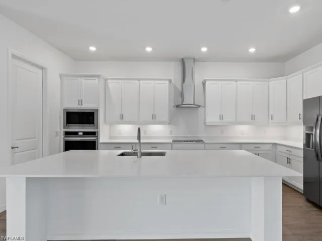 Kitchen with white cabinets, a kitchen island with sink, wall chimney exterior exhaust hood, appliances with stainless steel finishes, and a sink