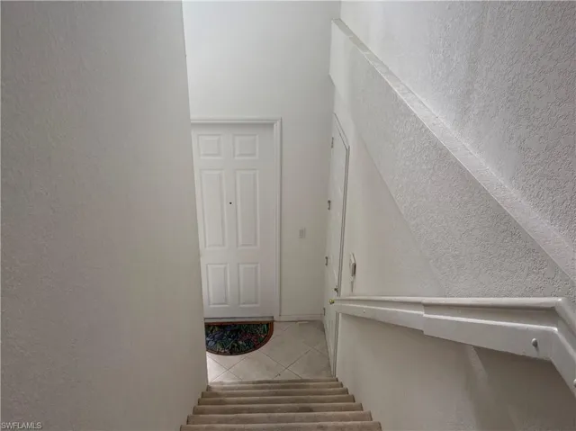 Entryway featuring a paneled door with a peephole, light-toned walls, and a staircase with a carpeted runner and a white handrail