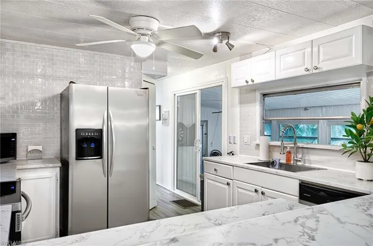 Kitchen with light stone countertops, appliances with stainless steel finishes, white cabinets, sink, and ceiling fan