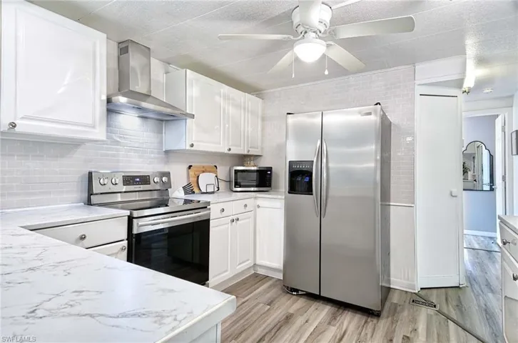 Kitchen with appliances with stainless steel finishes, white cabinetry, wall chimney exhaust hood, and light hardwood / wood-style flooring