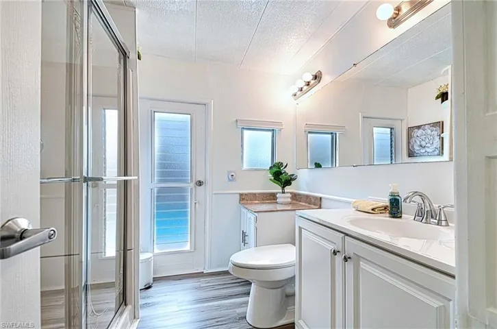 Bathroom with wood-type flooring, a shower with door, a textured ceiling, toilet, and vanity
