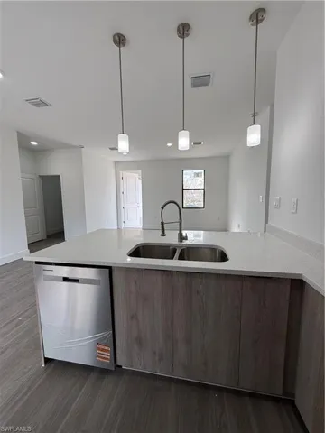 Kitchen featuring pendant lighting, light stone counters, dishwashing machine, open floor plan, and dark wood-type flooring