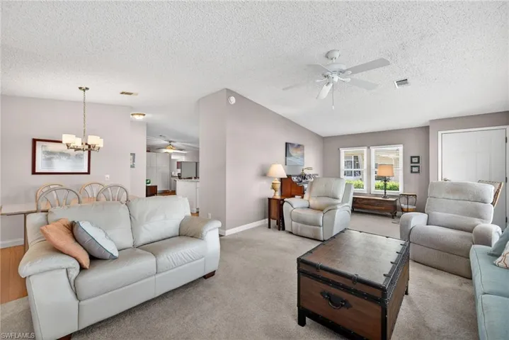 Living area with ceiling fan, carpet, lofted ceiling, a chandelier, and a textured ceiling
