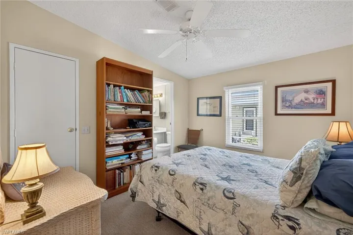 Carpeted bedroom with a textured ceiling, a ceiling fan, connected bathroom, and vaulted ceiling