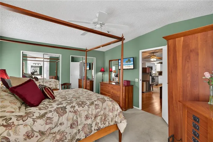 Carpeted bedroom with two closets, a textured ceiling, ceiling fan, and vaulted ceiling