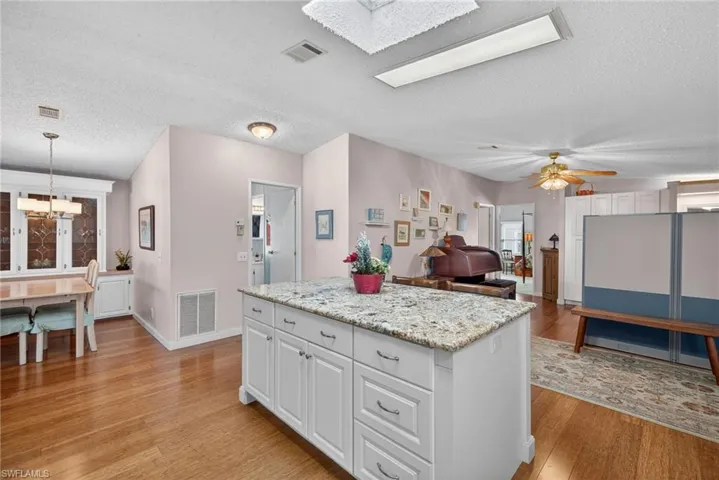 Kitchen with a kitchen island, a textured ceiling, white cabinets, light stone countertops, and a skylight