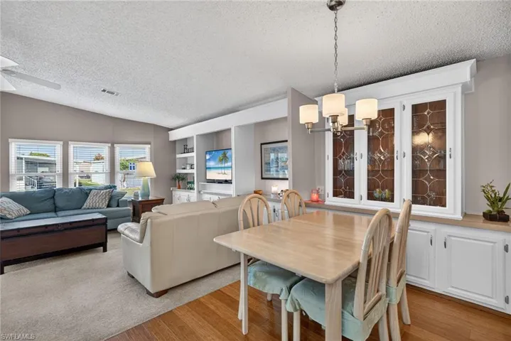 Dining room featuring a textured ceiling, a chandelier, lofted ceiling, light wood-style floors, and built in shelves