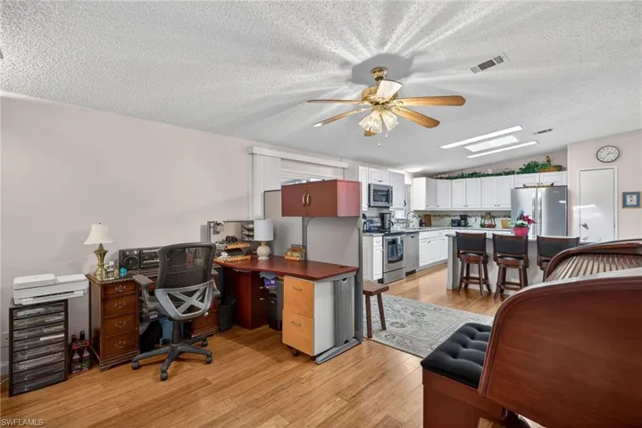 Office space with a textured ceiling, vaulted ceiling, light wood-style floors, and a ceiling fan