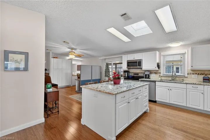 Kitchen featuring white cabinets, a skylight, light stone counters, a textured ceiling, and a center island
