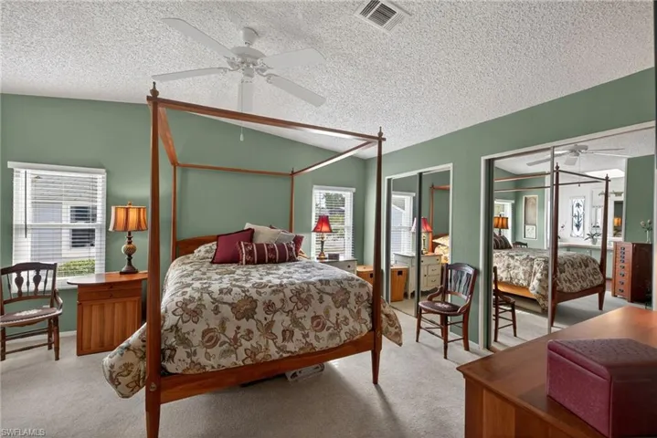 Bedroom featuring lofted ceiling, multiple closets, a textured ceiling, ceiling fan, and carpet