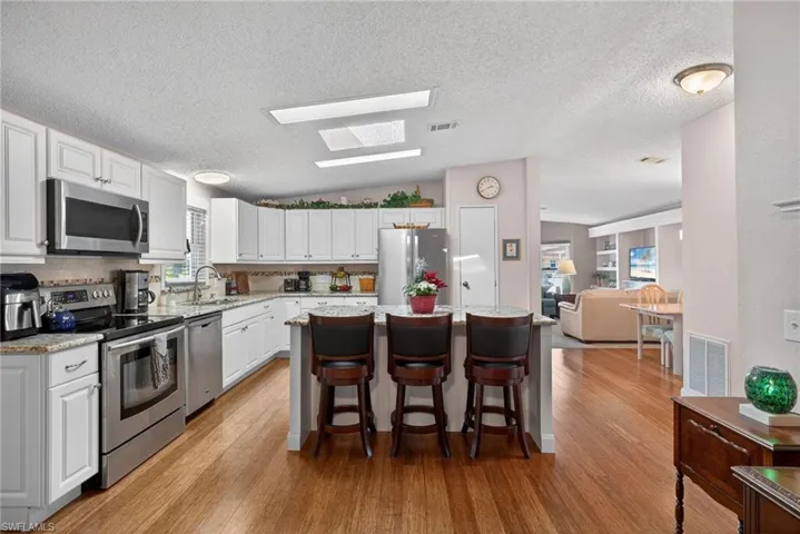 Kitchen with appliances with stainless steel finishes, a skylight, white cabinetry, a kitchen island, and lofted ceiling