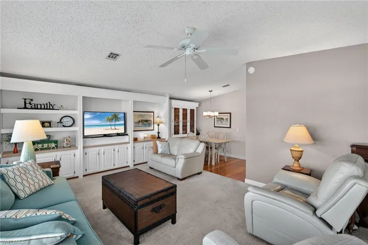 Living room featuring a textured ceiling, ceiling fan, built in shelves, and lofted ceiling