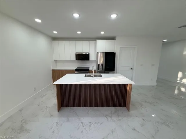 Kitchen with an island with sink, stainless steel appliances, recessed lighting, modern cabinets, and light stone countertops