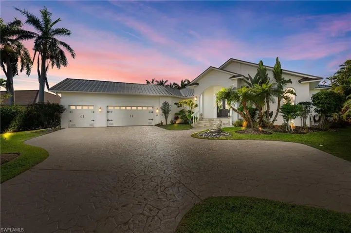View of front of house with stucco siding, a garage, metal roof, and driveway