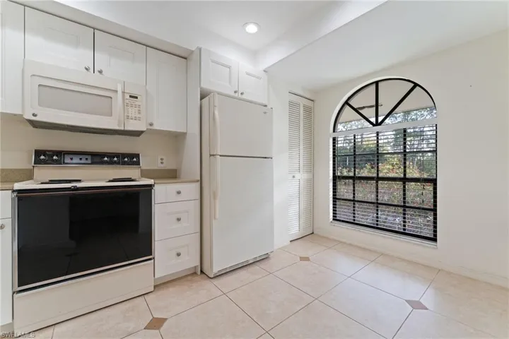 Kitchen featuring white appliances, white cabinets, light tile patterned floors, and recessed lighting