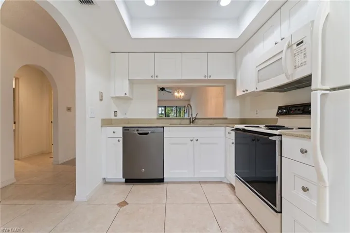 Kitchen featuring white appliances, white cabinets, arched walkways, and light tile patterned floors