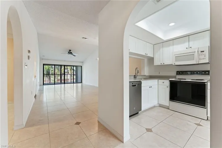 Kitchen with white appliances, arched walkways, white cabinets, light countertops, and a textured ceiling