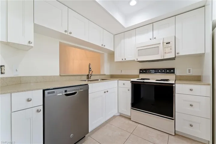 Kitchen with white appliances, white cabinetry, light stone countertops, light tile patterned flooring, and recessed lighting