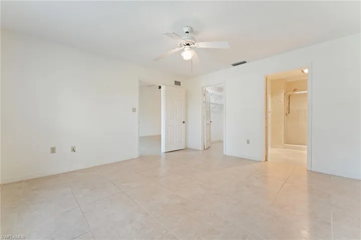 Unfurnished bedroom with a ceiling fan, a spacious closet, light tile patterned floors, and connected bathroom