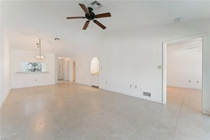 Unfurnished living room featuring light tile patterned floors, vaulted ceiling, ceiling fan, arched walkways, and a chandelier