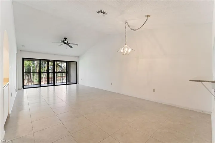 Unfurnished room with vaulted ceiling, light tile patterned flooring, a textured ceiling, a chandelier, and a ceiling fan