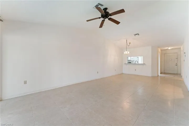 Unfurnished living room featuring ceiling fan, light tile patterned floors, vaulted ceiling, and a chandelier