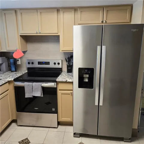 Kitchen with stainless steel appliances, light stone countertops, light tile patterned flooring, and decorative backsplash