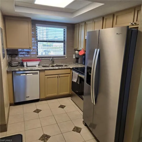 Kitchen with stainless steel appliances, light tile patterned floors, light stone countertops, and light brown cabinetry