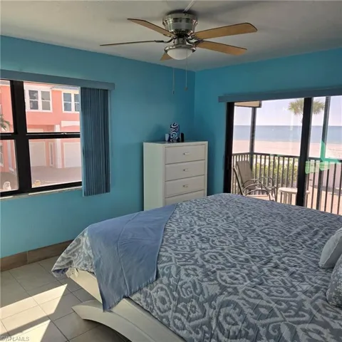 Tiled bedroom with access to exterior, a ceiling fan, a water view, and multiple windows