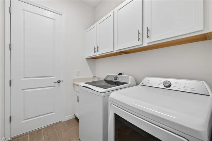 The laundry area features white cabinetry with silver hardware, a light wooden shelf, and a light-colored countertop