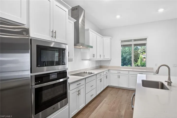 Kitchen featuring white cabinetry, stainless steel appliances, light countertops, and wood-style flooring