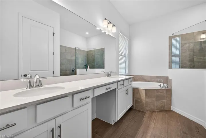 Primary Bathroom featuring dual undermount sinks with chrome fixtures, a large vanity mirror, and a corner soaking tub with tiled surround
